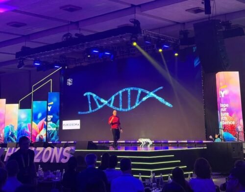 Engel Fonseca en el escenario de EY Horizons 2026 frente a una pantalla con una hélice de ADN y el logo de Curioxoma