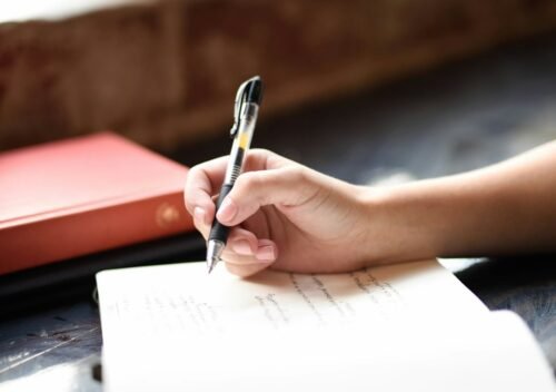 Mano escribiendo con pluma en un cuaderno junto a una ventana