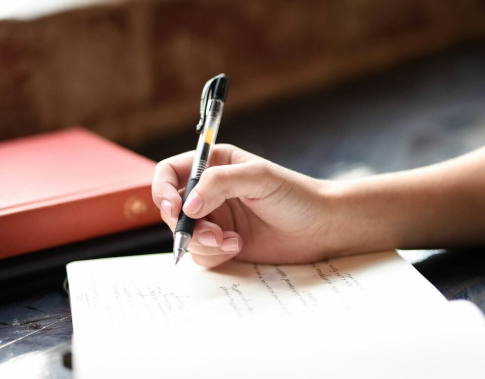 Mano escribiendo con pluma en un cuaderno junto a una ventana